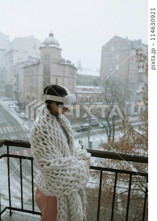 A beautiful girl in virtual reality glasses against the backdrop of a winter cityscape. 114630921