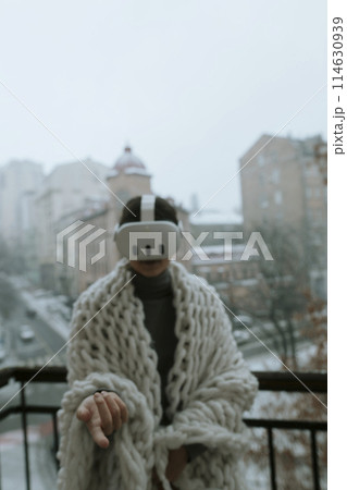 A young woman in a virtual reality headset stands on the balcony in winter. A young woman in a virtual reality headset stands on the balcony in winter. 114630939