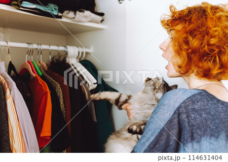 red-haired teenage girl and big cat choose things from closet 114631404