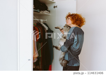 red-haired teenage girl and big cat choose things from closet 114631406