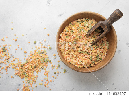 Wooden bowl with scoop of dry raw green and orange peas seeds on light table. 114632407