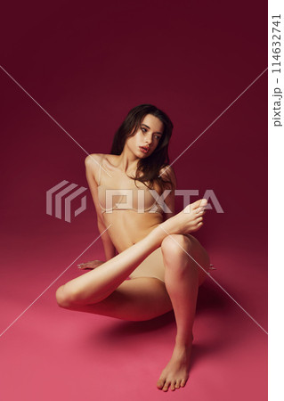 Beautiful young brunet girl with slim perfect body shape posing in beige underwear against magenta studio background Beautiful young brunet girl with slim perfect body shape posing in beige underwear against magenta studio background 114632741
