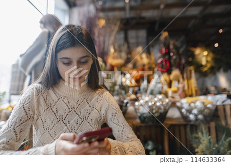 A striking, vibrant young woman checking out New Year's decorations with her smartphone. 114633364
