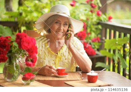 Happy aged woman drinking coffee and talking on phone 114635136