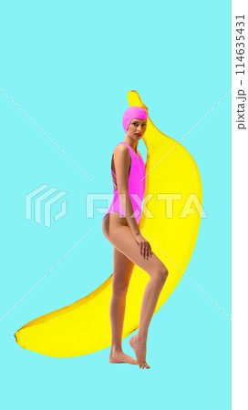 Young girl in pink swimsuit and cap posing with a giant banana against a turquoise background. Contemporary art collage. 114635431
