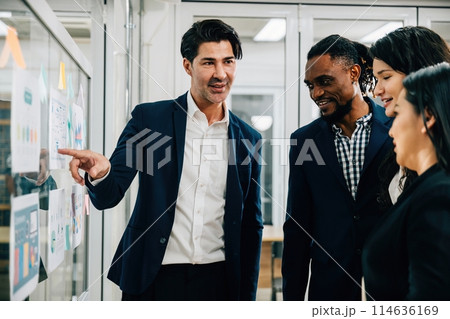 A team of professionals gathers in a boardroom meeting, brainstorming and planning on a glass wall. Their collaboration and creative thinking are vital to the success of their business startup. 114636169