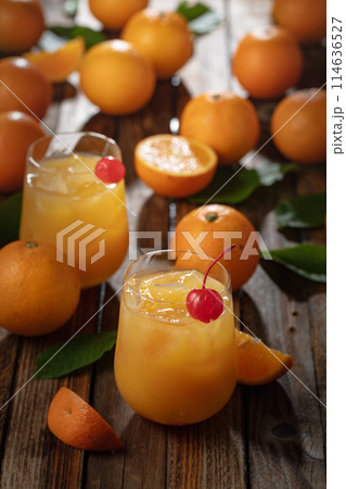 Orange juice with ice garnished with red cherry. 114636527
