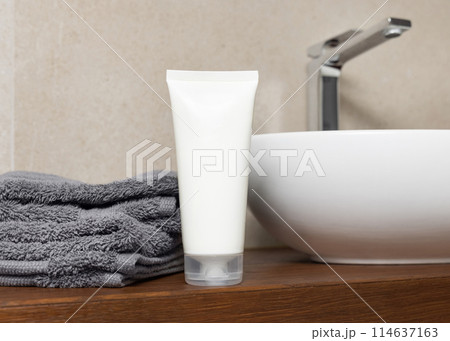 White cosmetic tube near grey folded towels and basin on wooden countertop in bath, mockup White cosmetic tube near grey folded towels and basin on wooden countertop in bath, mockup 114637163