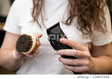 Hairdresser holding brush and hair clipper, closeup.  114637288