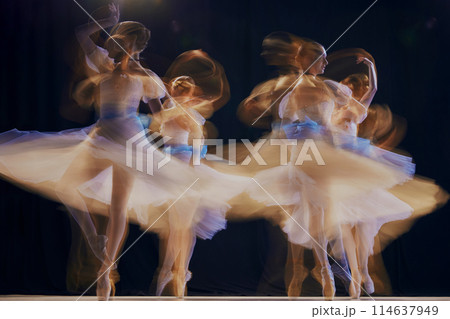 Young ballet ensemble in sheer dresses creating illusion of multiple movements against a dark background on stage. 114637949
