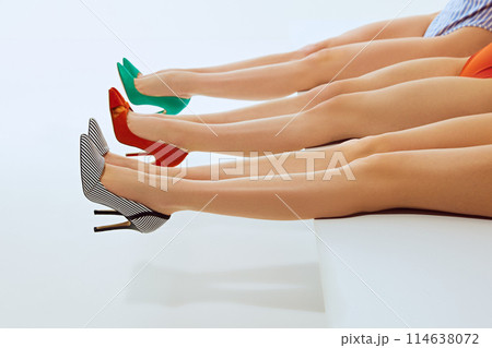 Creative image of female legs of three models wearing colorful high heels, against white background. Highlighting fashion and elegance in footwear. Creative image of female legs of three models wearing colorful high heels, against white background. Highlighting fashion and elegance in footwear. 114638072