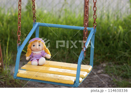 Little hand made doll seating on yellow wooden bench in bright summer day Little hand made doll seating on yellow wooden bench in bright summer day 114638336