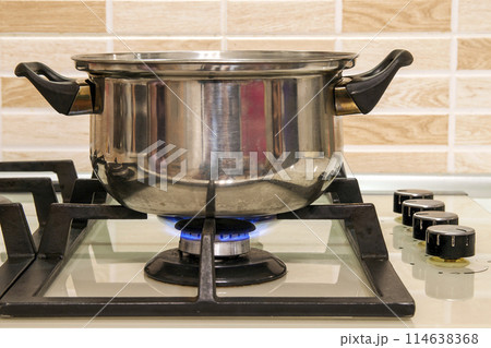 Metal cooking pot standing on kitchen stove with flame. Metal cooking pot standing on kitchen stove with flame. 114638368