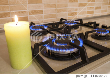 Closeup shot of blue fire from domestic kitchen stove. Gas cooker with burning flames propane gas and candle. Old and new concept 114638379