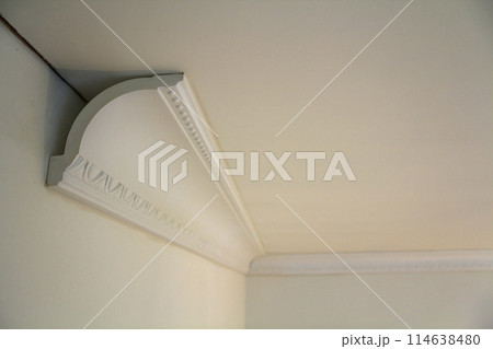 Close-up detail of decoration white molding connected with glue adhesive to wall and ceiling in interior room renovation and reconstruction. 114638480