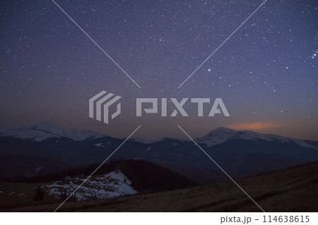 Majestic view of fantastic starry dark sky over magnificent Carpathian mountains covered with evergreen forest and snow-capped peaks in distance. Breathtaking panorama of beauty and magic of nature. Majestic view of fantastic starry dark sky over magnificent Carpathian mountains covered with evergreen forest and snow-capped peaks in distance. Breathtaking panorama of beauty and magic of nature. 114638615