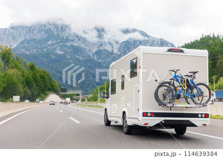 Scenic view big modern white family rv camper van vehicle drive Europe highway road alpine mountain cloud in summer day. Rving motorhome lifestyle travel and adventure tourism trip journey concept Scenic view big modern white family rv camper van vehicle drive Europe highway road alpine mountain cloud in summer day. Rving motorhome lifestyle travel and adventure tourism trip journey concept 114639384