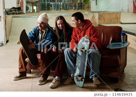 Group of joyful Caucasian boys and girl hanging out together sitting on old couch in skatepark and chatting 114639435