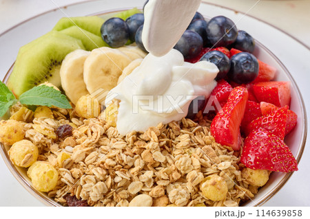 Granola with strawberries, kiwi, banana and blueberries in a round plate topped with yogurt on the table. Healthy and tasty food 114639858