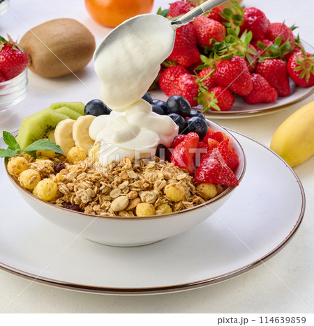 Granola with strawberries, kiwi, banana and blueberries in a round plate on a white table. Healthy and tasty food 114639859