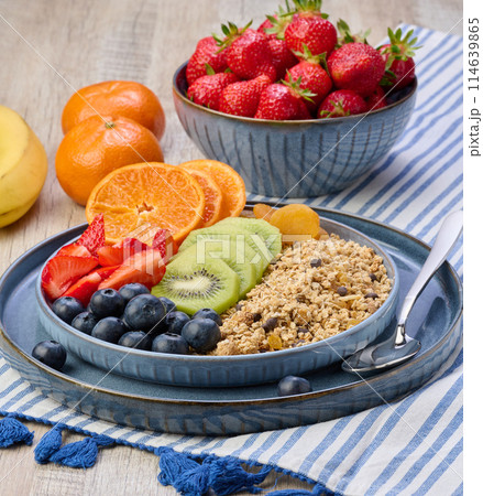 Granola with strawberries, kiwi, banana and blueberries in a round plate on a white table. Granola with strawberries, kiwi, banana and blueberries in a round plate on a white table. 114639865