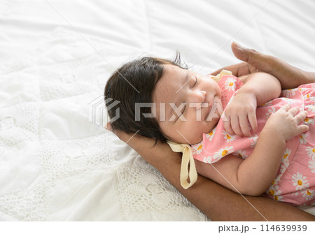 Cute Asian newborn baby girl  sleeping on dad hand. Father nursing his infant with love on bed at home. Love and new life concept 114639939