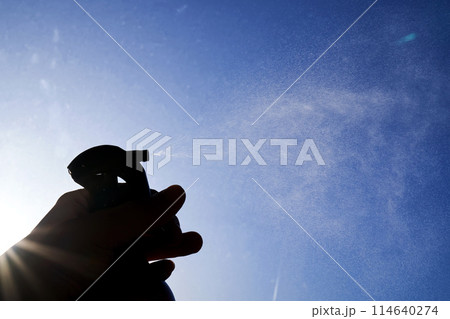 A woman's hand sprays an air freshener against the sky. A woman's hand sprays an air freshener against the sky. 114640274