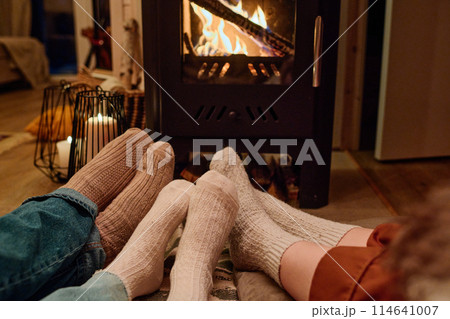 Feet in socks of unrecognizable family of three sitting on floor in front of fireplace in their cottage, copy space 114641007