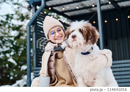 Low angle view shot cheerful Caucasian girl wearing eyeglasses spending winter day outdoors with her lagotto romagnolo dog Low angle view shot cheerful Caucasian girl wearing eyeglasses spending winter day outdoors with her lagotto romagnolo dog 114641058