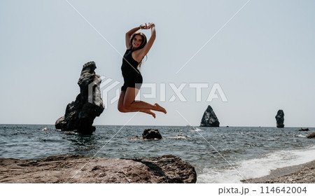 Woman summer travel sea. Happy tourist in hat enjoy taking picture outdoors for memories. Woman traveler posing on the beach at sea surrounded by volcanic mountains, sharing travel adventure journey 114642004