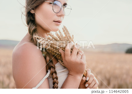Woman wheat field. Agronomist, Woman farmer check golden ripe barley spikes in cultivated field. A woman is holding a bunch of wheat in her arms. Woman wheat field. Agronomist, Woman farmer check golden ripe barley spikes in cultivated field. A woman is holding a bunch of wheat in her arms. 114642005