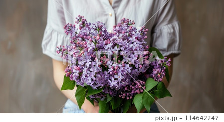 Gentle hands of a woman in a white dress cradle a lush bouquet of lilac Gentle hands of a woman in a white dress cradle a lush bouquet of lilac 114642247