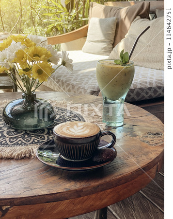 A cup of coffee with latte art on top on wooden table with mango smoothie A cup of coffee with latte art on top on wooden table with mango smoothie 114642751