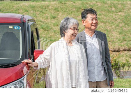 ドライブ・旅行に来た自動車の前に立つ笑顔のシニア夫婦 ドライブ・旅行に来た自動車の前に立つ笑顔のシニア夫婦 114645482