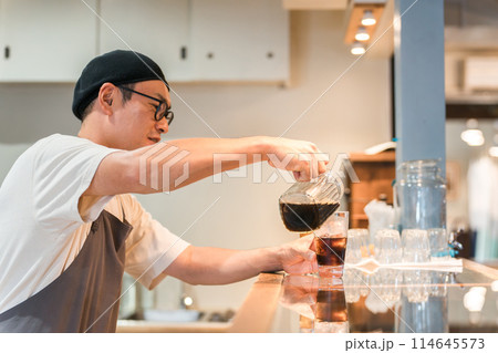 カフェ・飲食店のカウンターでコーヒをグラスに注ぐ店員・キッチンスタッフの男性 114645573