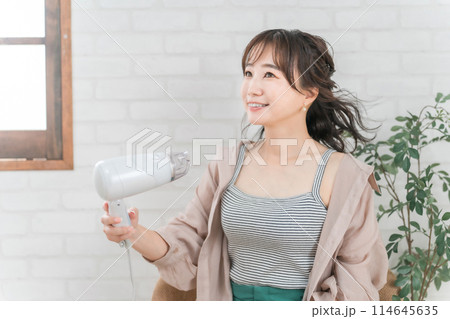 部屋でドライヤーを使ってヘアブローする女性 114645635