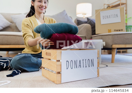 Young Asian women sit in living room sorting clothes for donation in a donation box second hand clothes Young Asian women sit in living room sorting clothes for donation in a donation box second hand clothes 114645834