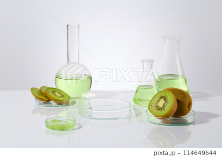 Plenty lab glassware containing kiwi and light green essence placed surround a blank petri dish in the center for displaying products extracted from kiwi. Frontal shot, blank space for adding text Plenty lab glassware containing kiwi and light green essence placed surround a blank petri dish in the center for displaying products extracted from kiwi. Frontal shot, blank space for adding text 114649644