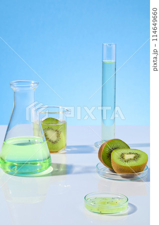 Creative photo for promotion was shot from front, the white flat against blue background with gradient effect, erlenmeyer flask and measuring cylinder with light green fluid and fresh kiwi 114649660