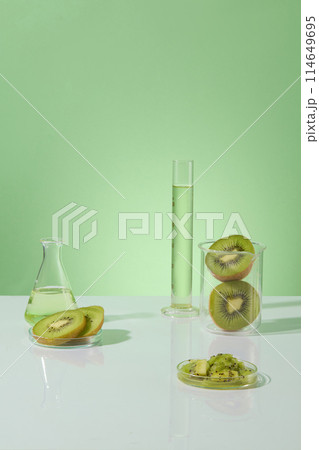 Green background features kiwis contained inside a beaker and petri dishes. Liquid in green color filled inside glassware. Kiwis can reduce tiredness and improve energy levels 114649695