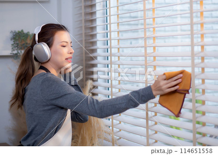 Excited young asian woman with headphones singing and dancing while dusting a window. Excited young asian woman with headphones singing and dancing while dusting a window. 114651558