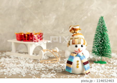 Small snowman with white sleigh and christmas tree on grey background 114652463