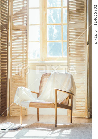 Wooden armchair with plaid against windows with shutters , room composition and sunlight Wooden armchair with plaid against windows with shutters , room composition and sunlight 114655502