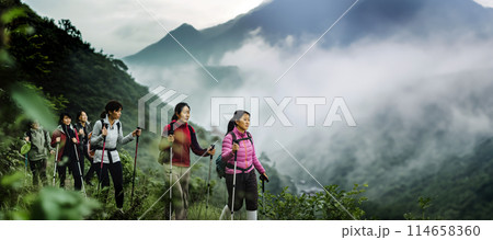 A group of middle-aged Chinese women go hiking in the mountains with Nordic walking poles, it has just rained heavily and there is fog in the mountains, promoting an active lifestyle. 114658360