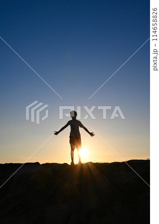 夕日に照らされる手を広げた少年のシルエット 114658826