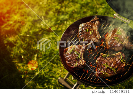 top view of grill with ribeye steaks grilling in the backyard of a house, barbecue party on a bright sunny day, party invitation poster top view of grill with ribeye steaks grilling in the backyard of a house, barbecue party on a bright sunny day, party invitation poster 114659151