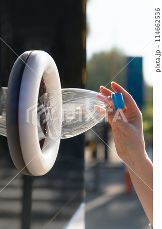 Woman uses a self service machine to receive used plastic bottles and cans on a city street.. Woman uses a self service machine to receive used plastic bottles and cans on a city street.. 114662536