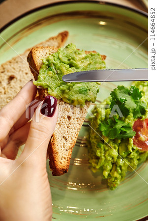 Female hands spreading guacamole on slice of toasted bread 114664852