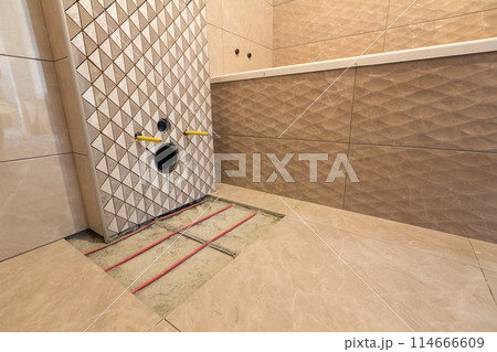 Unfinished reconstruction of bathroom with ceramic tiles installed on walls, heating electrical cables system on cement floor and place for toilet. 114666609