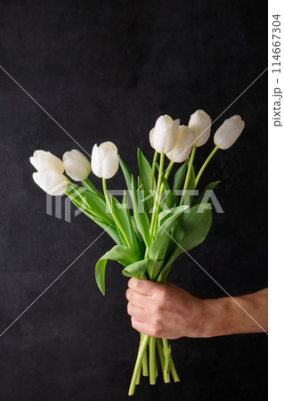 A male hand holds a bouquet of white tulips 114667304